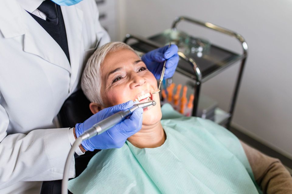Un dentista in camice bianco e guanti blu esegue una visita odontoiatrica su un paziente seduto sulla poltrona dello studio.