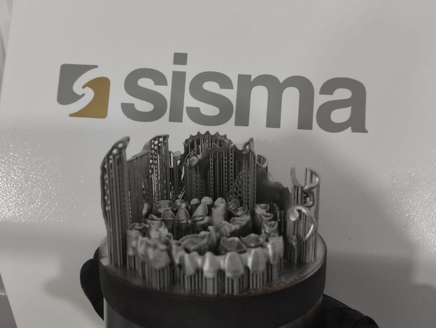 Una struttura dentale in metallo stampata in 3D, composta da diverse corone dentali fissate a una base, con lo sfondo del logo Sisma.