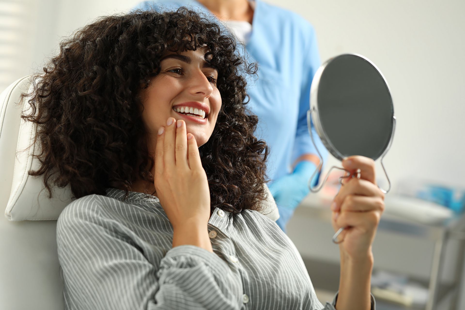 Woman smiling and checking her teeth in a hand mirror at a dental office.