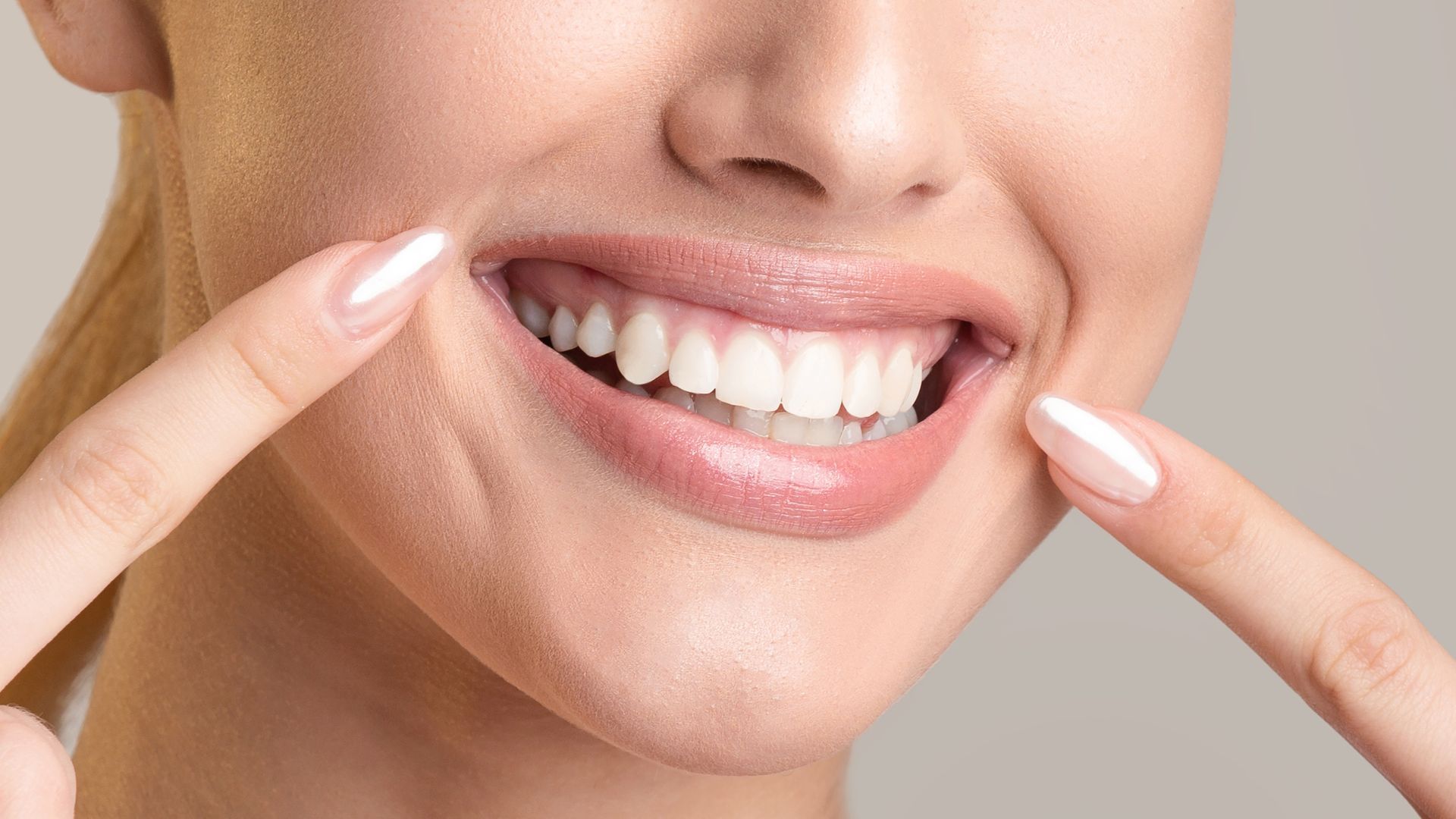 Woman smiling, pointing to her bright, white teeth.