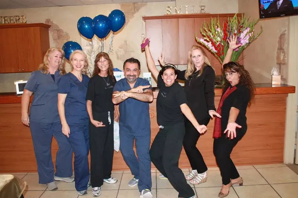 Group of dental staff celebrating, blue balloons in background. Smiles and raised arms.