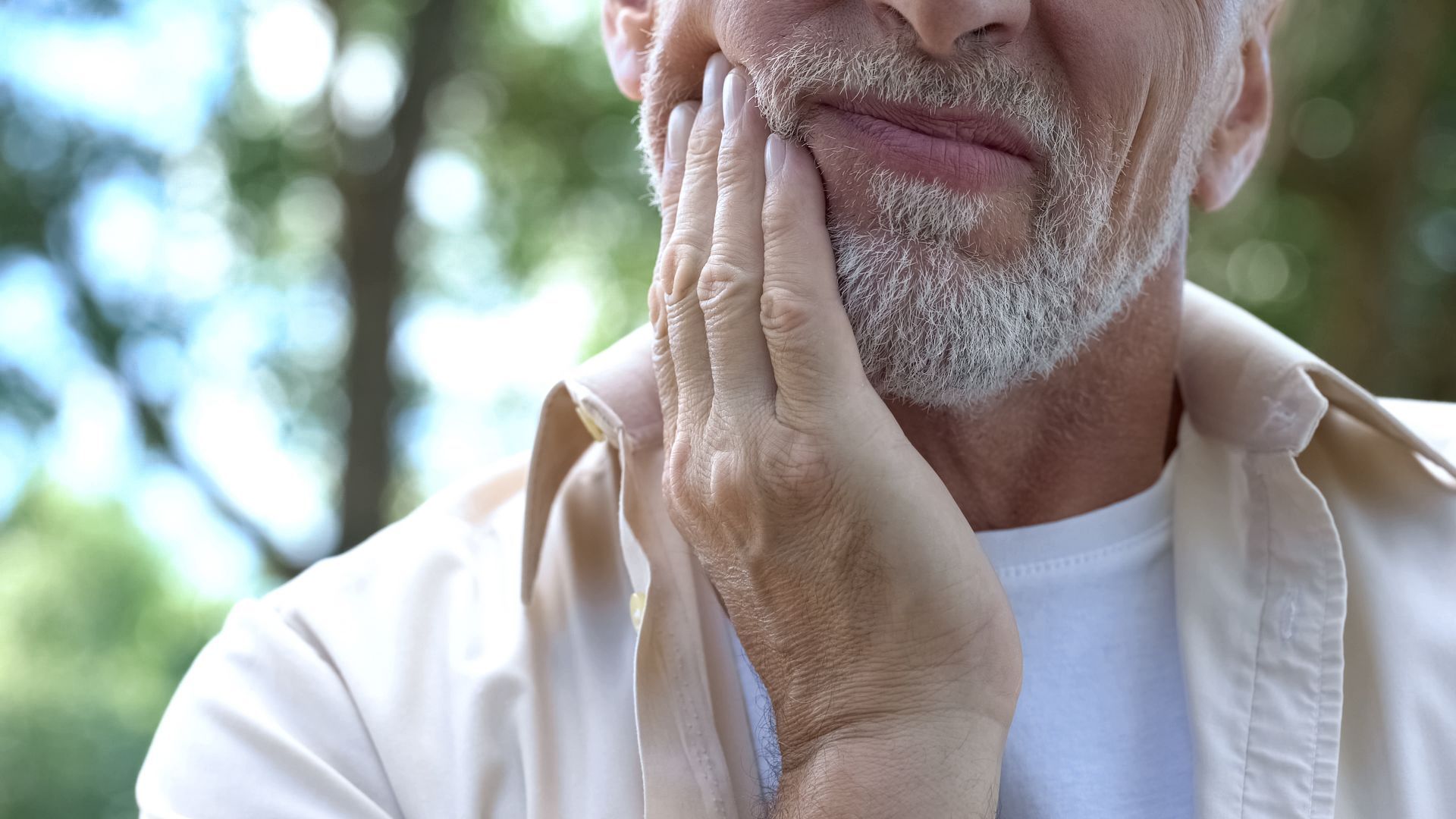 Man holding cheek, displaying an expression of pain, outdoors.