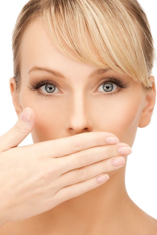 Woman with blonde hair, hand covering her mouth, eyes looking forward.