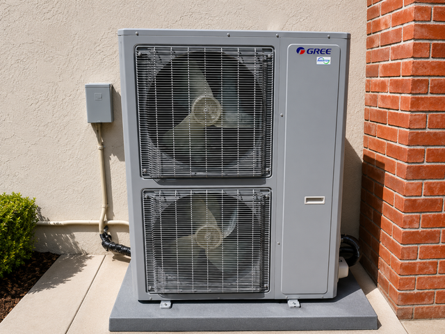 Outdoor HVAC unit beside a brick wall and beige building exterior
