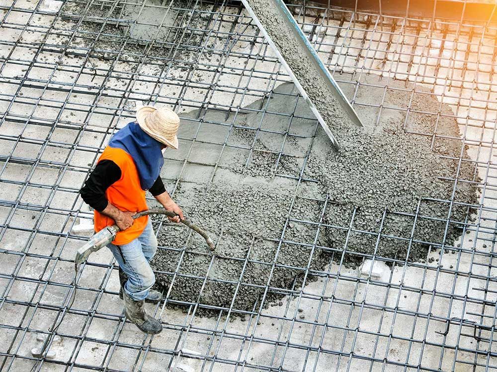 Top view of builders in orange shirt pouring concrete works on the construction site
