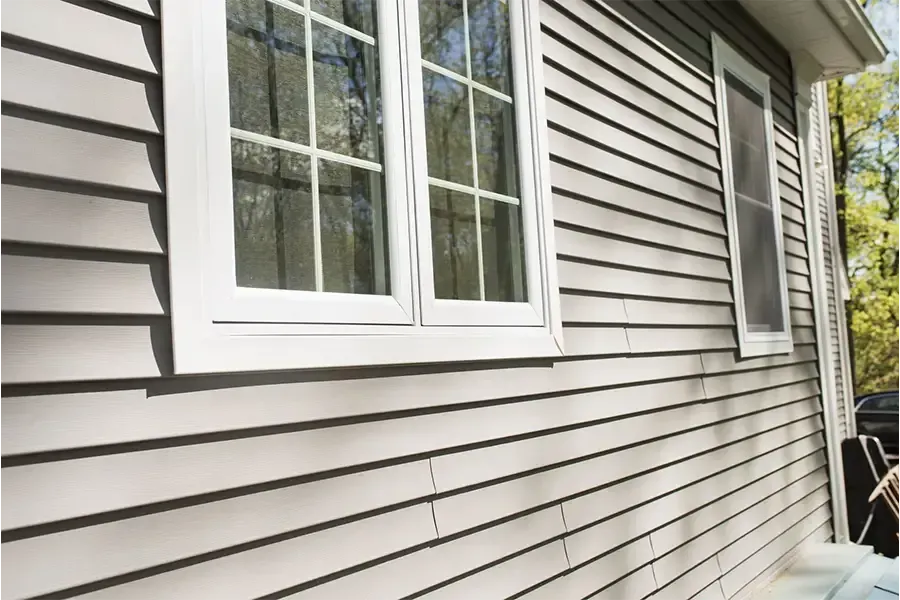 Gray vinyl siding on a house exterior with a white double window and a small side window under the roof eave