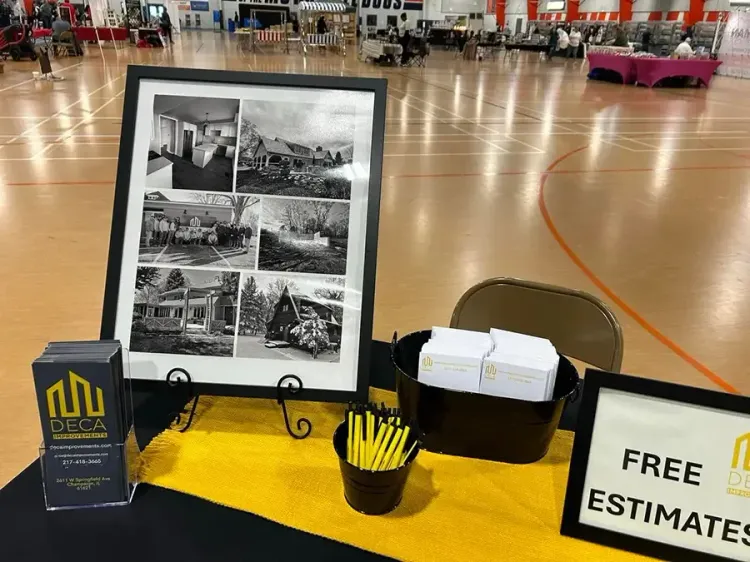 Trade show table with framed black-and-white photo collage, yellow cup, brochure box, and “FREE ESTIMATE” sign