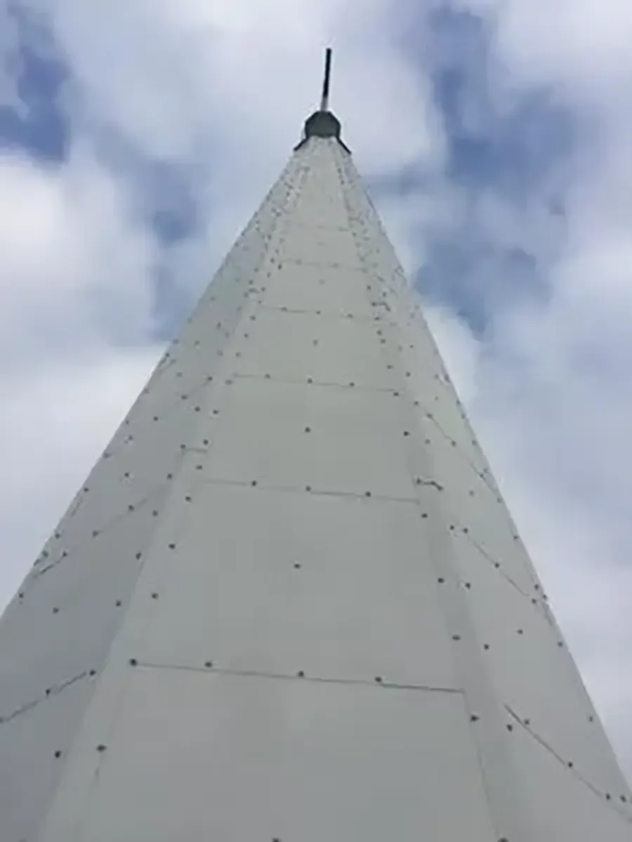 Looking up a tall white tower with a pointed spire against a cloudy sky