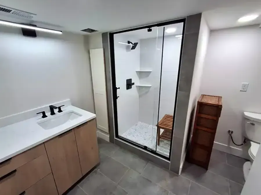 Modern bathroom with vanity sink, glass shower, gray tile floor, and wooden storage cabinet.
