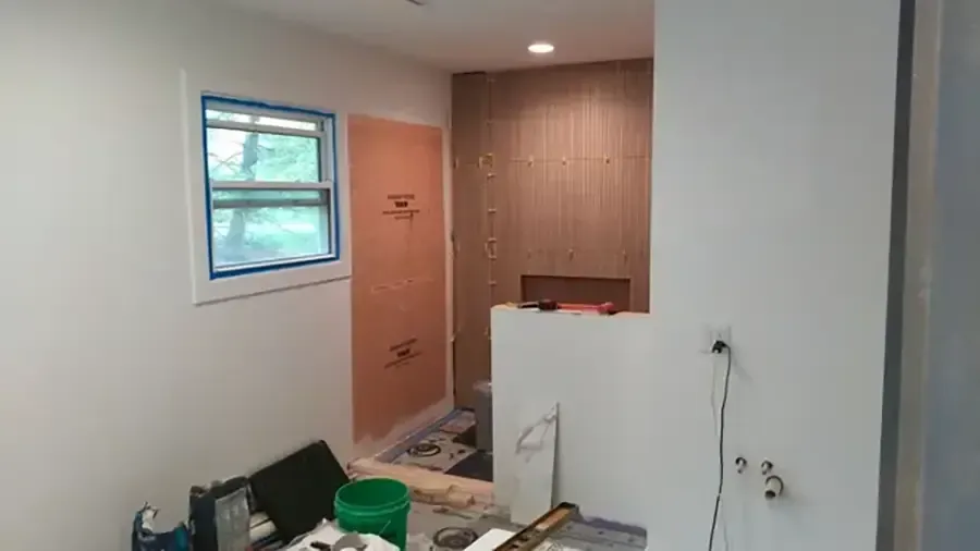 Small room under renovation with tools, a window, a door, and a partial wall against wood paneling.