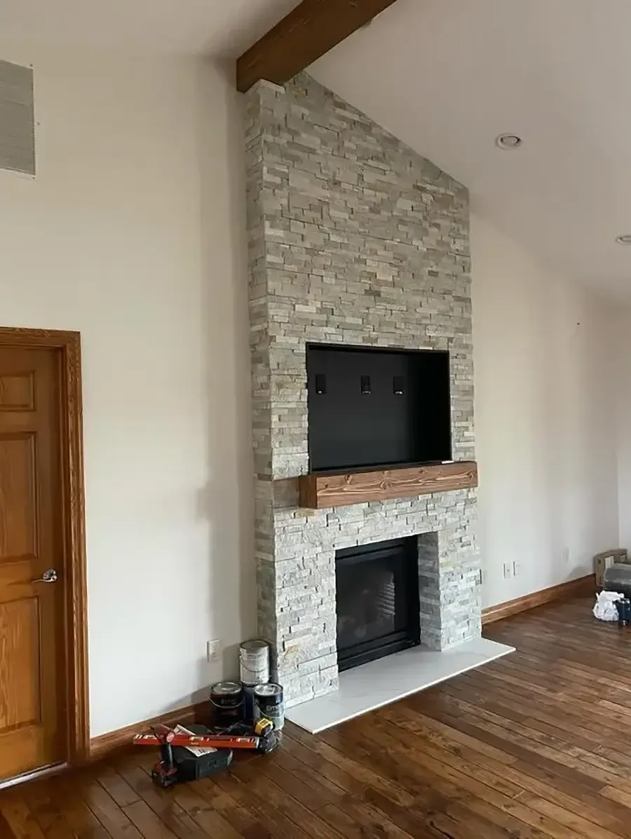 Living room fireplace with stone surround, wood mantel, and wall-mounted TV above hardwood floors