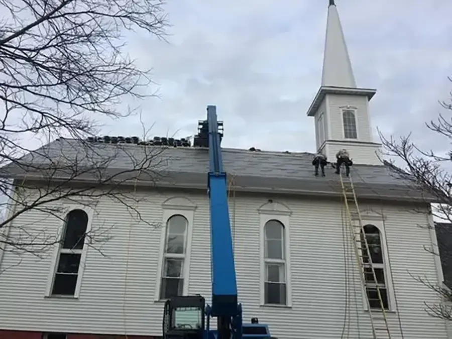 White church with tall steeple being serviced by a blue lift under a cloudy sky