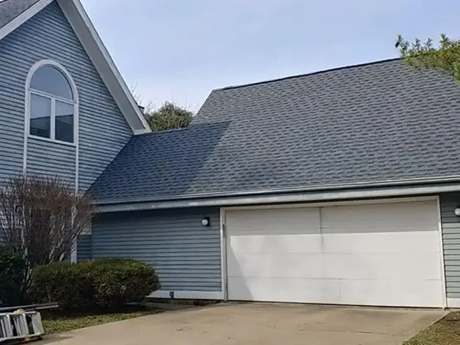 Blue house with white garage doors and arched window, viewed from the driveway.