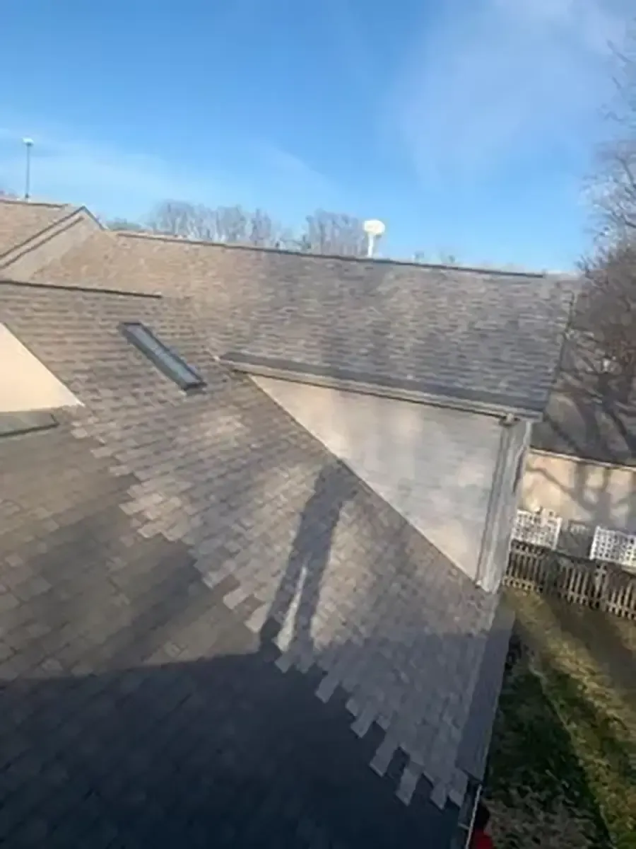 Roof with gray shingles, skylight, and chimney under a clear blue sky.
