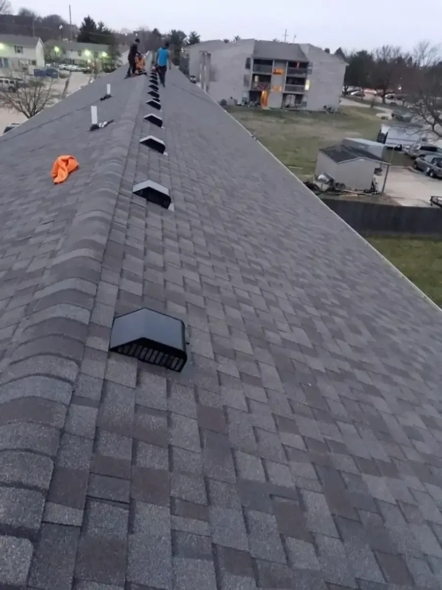 Workers on a shingled rooftop installing vents on a cloudy day