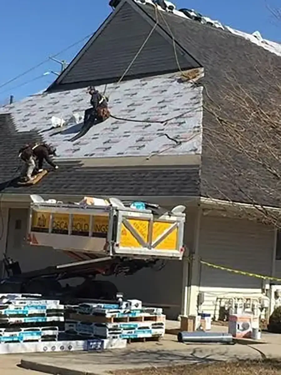 Roofers installing shingles on a house roof with a dumpster below.