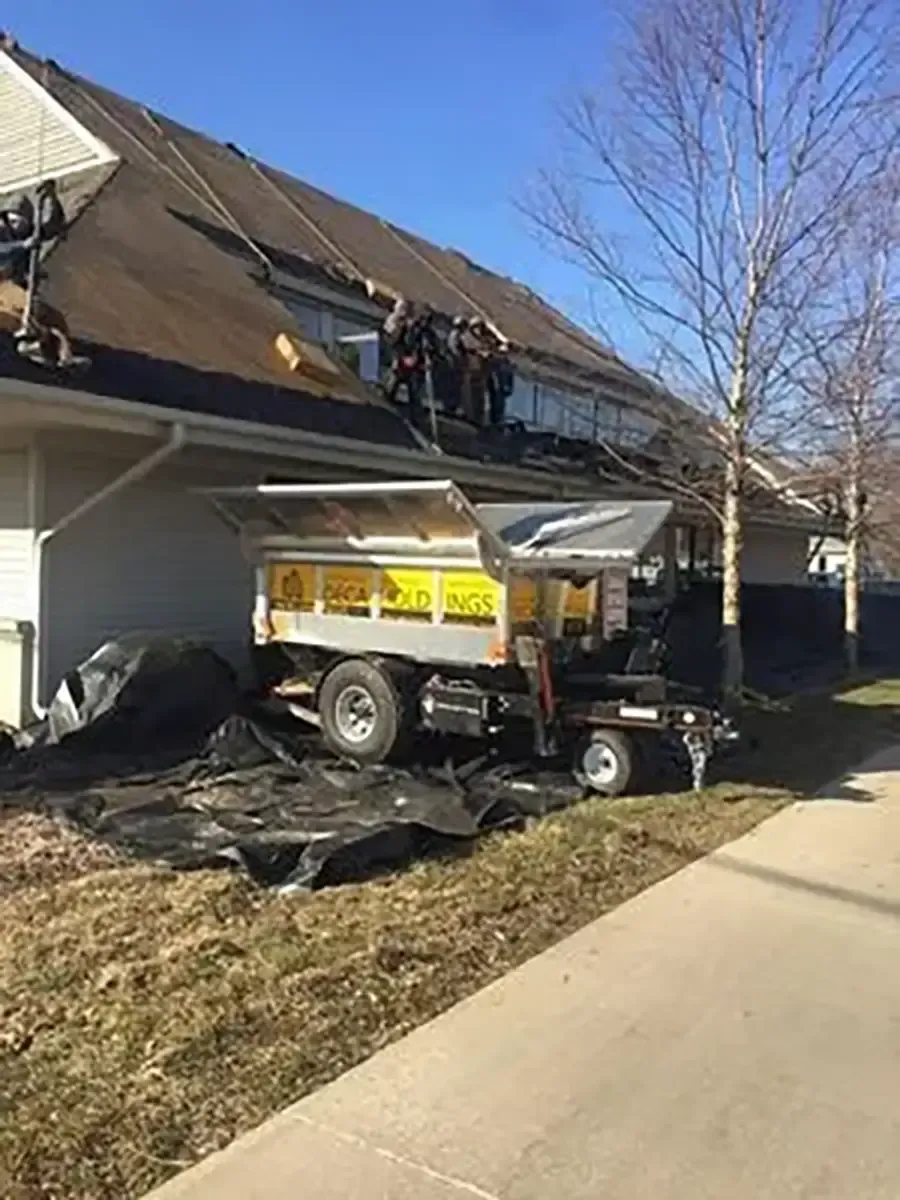 Utility truck parked beside a house with workers on the roof and debris on the ground