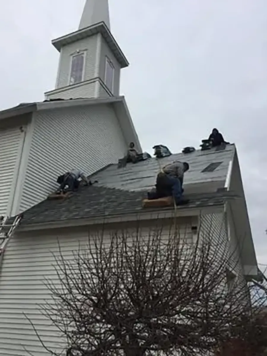 Workers repairing a church roof with shingles removed on a cloudy day