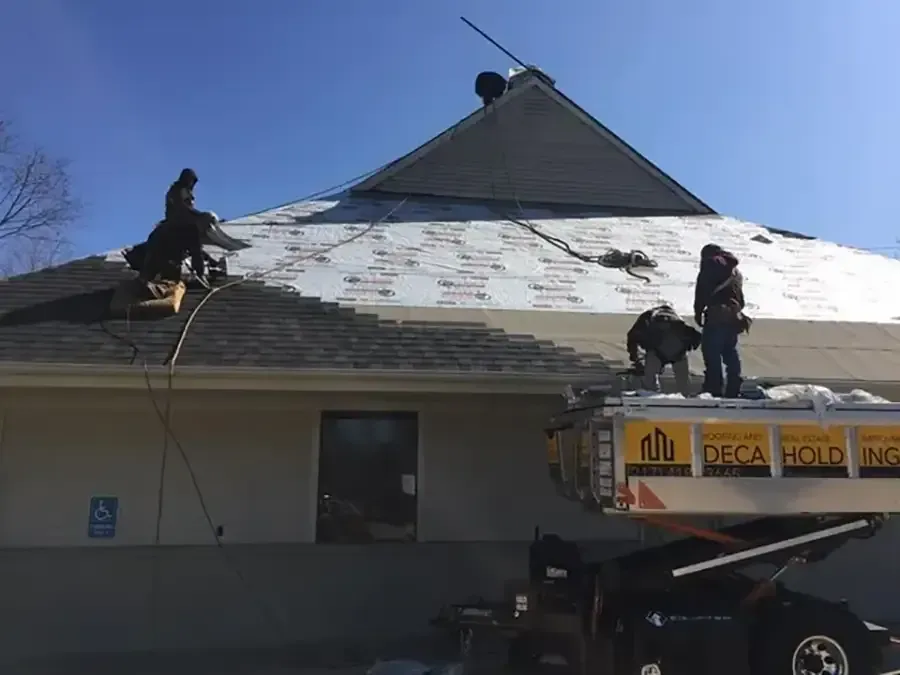 Workers repairing a snow-covered roof beside a lift truck and ladder under a blue sky
