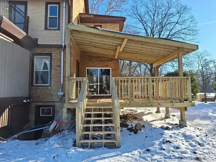 Snowy backyard porch with wooden stairs and covered deck attached to a house