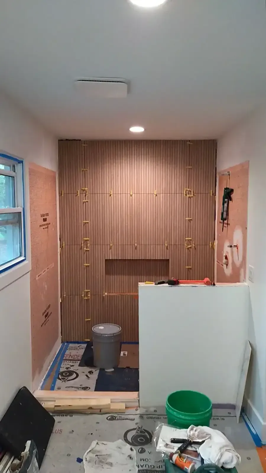 Narrow hallway with wood-paneled wall, small alcove, mirror, trash bin, and cleaning supplies on the floor.