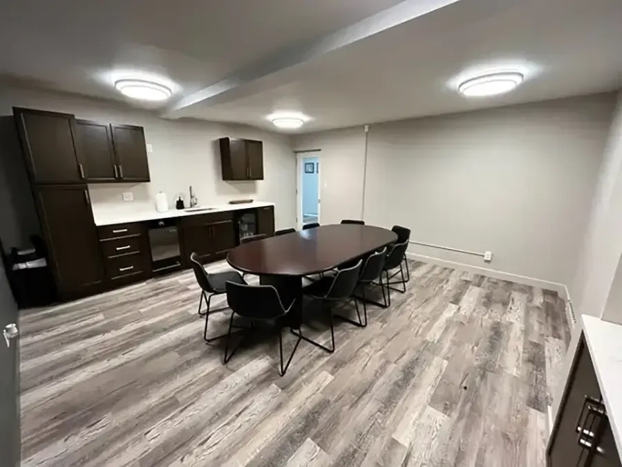 Modern kitchen-dining room with dark cabinets, wood floors, and a table surrounded by folding chairs.