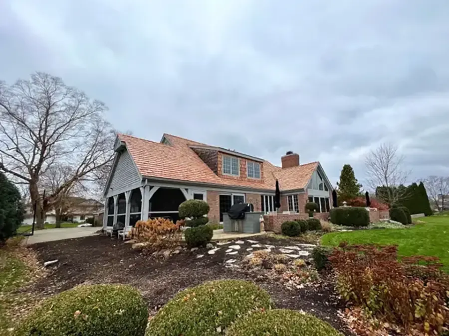 Stone house with red-tiled roof, arched porch, and landscaped front yard under a cloudy sky