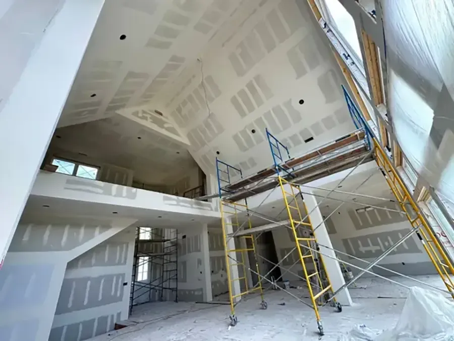 Interior of a drywall-finished room with tall ceilings, scaffolding, and ladder in a construction site