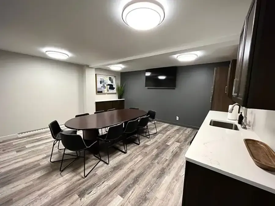 Modern conference room with oval table, black chairs, wall-mounted TV, and gray walls