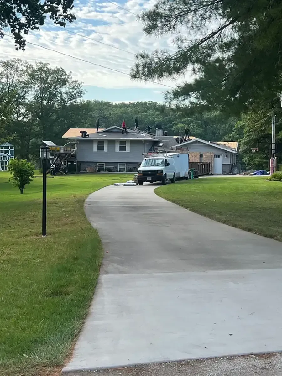 Curved driveway leading to a gray house with a white truck parked outside and trees overhead