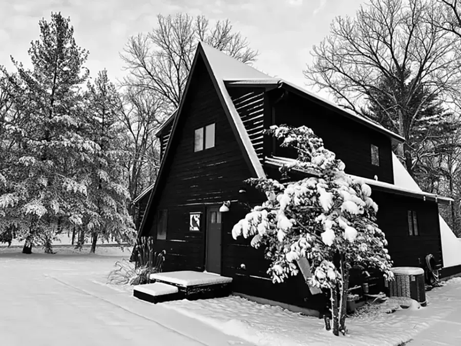 Snow-covered black house with steep roof and trees in a winter landscape