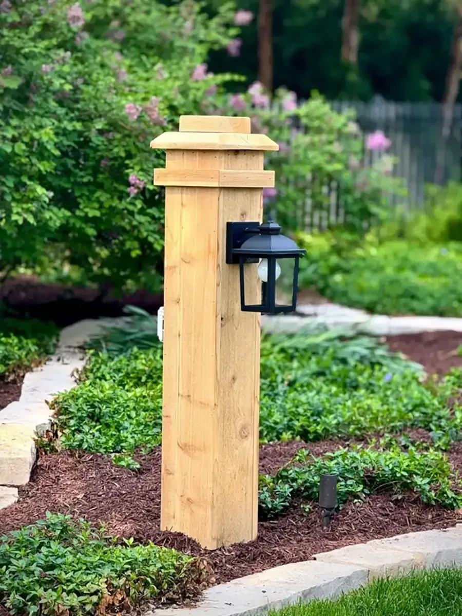 Wooden garden post with black lantern beside a landscaped path and greenery
