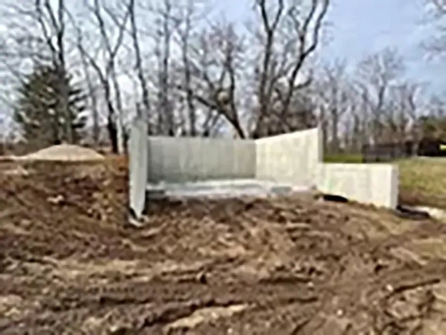 White fence panels on a dirt mound in a bare, wooded area under a cloudy sky