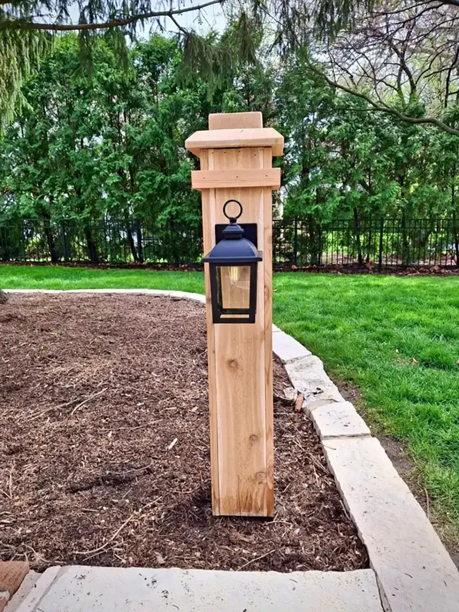 Wooden garden post with a black lantern, set beside a curved concrete border and mulch bed.