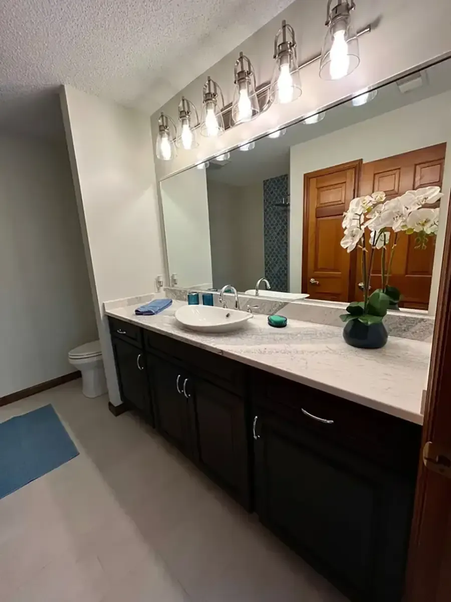 Bathroom vanity with large mirror, wall lights, and white countertop with orchid and toiletries
