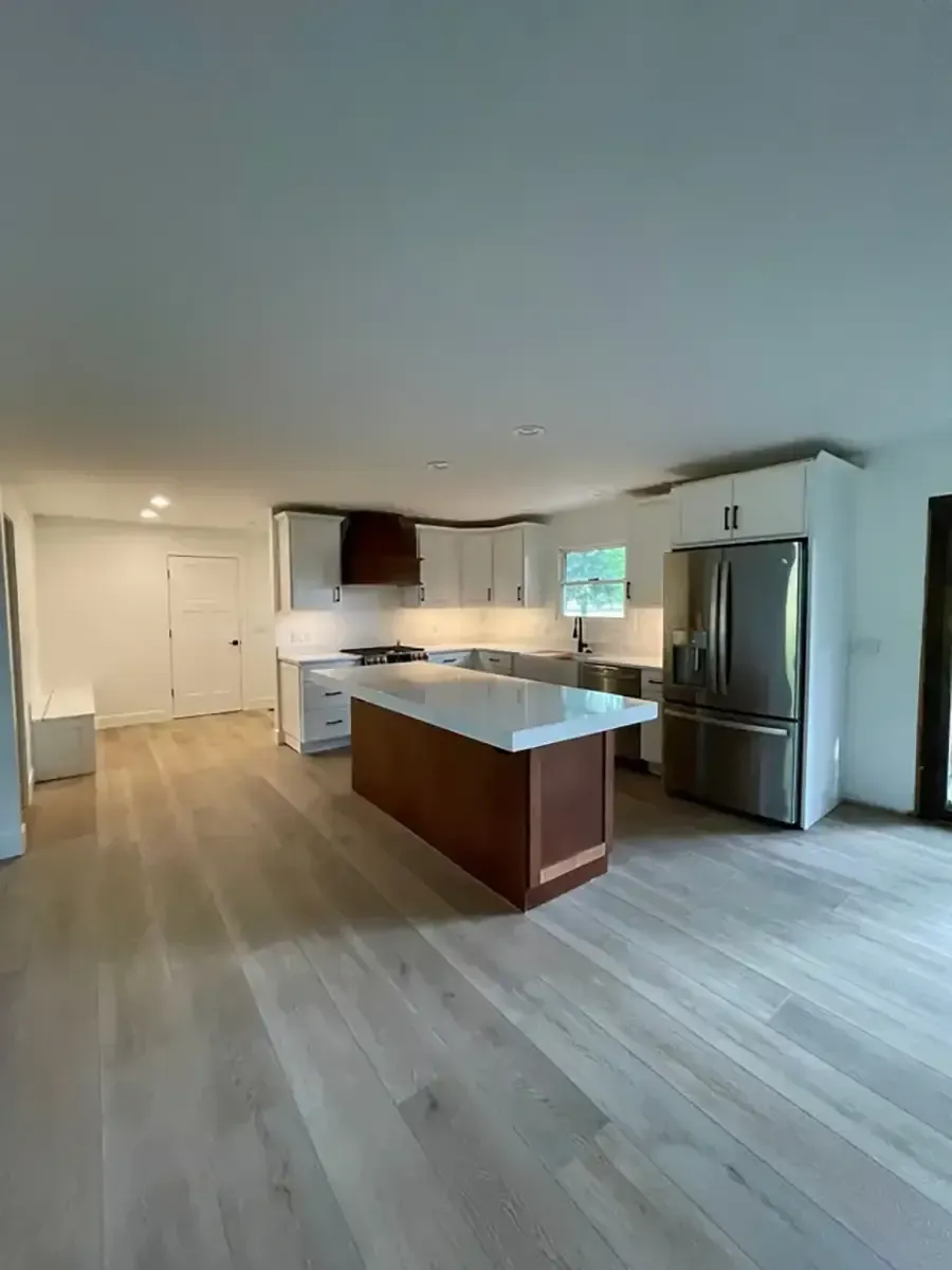 Modern kitchen with stainless steel fridge, island, white cabinets, and light wood flooring
