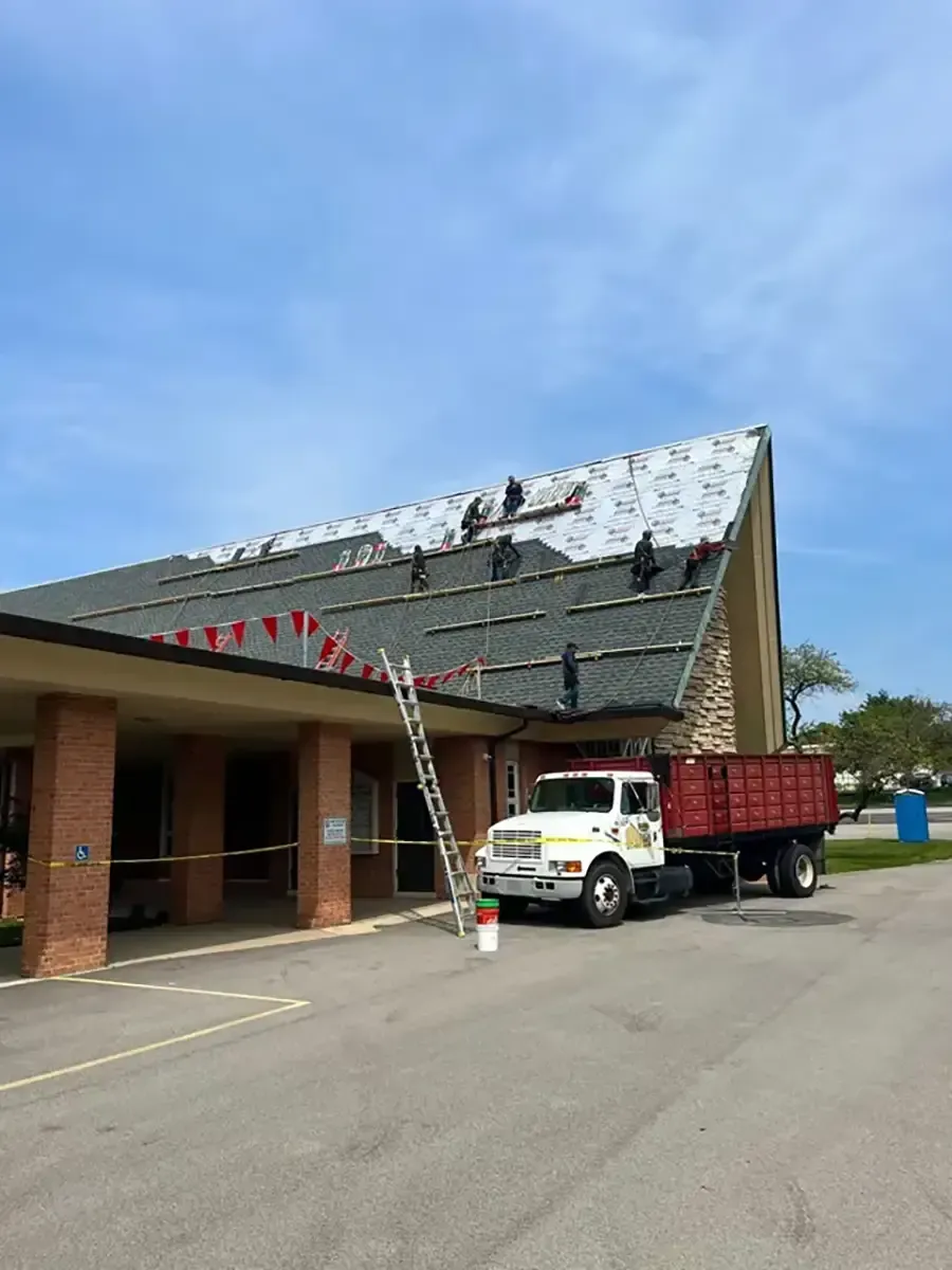Dump truck and white utility truck under a damaged building awning, with debris on the roof.