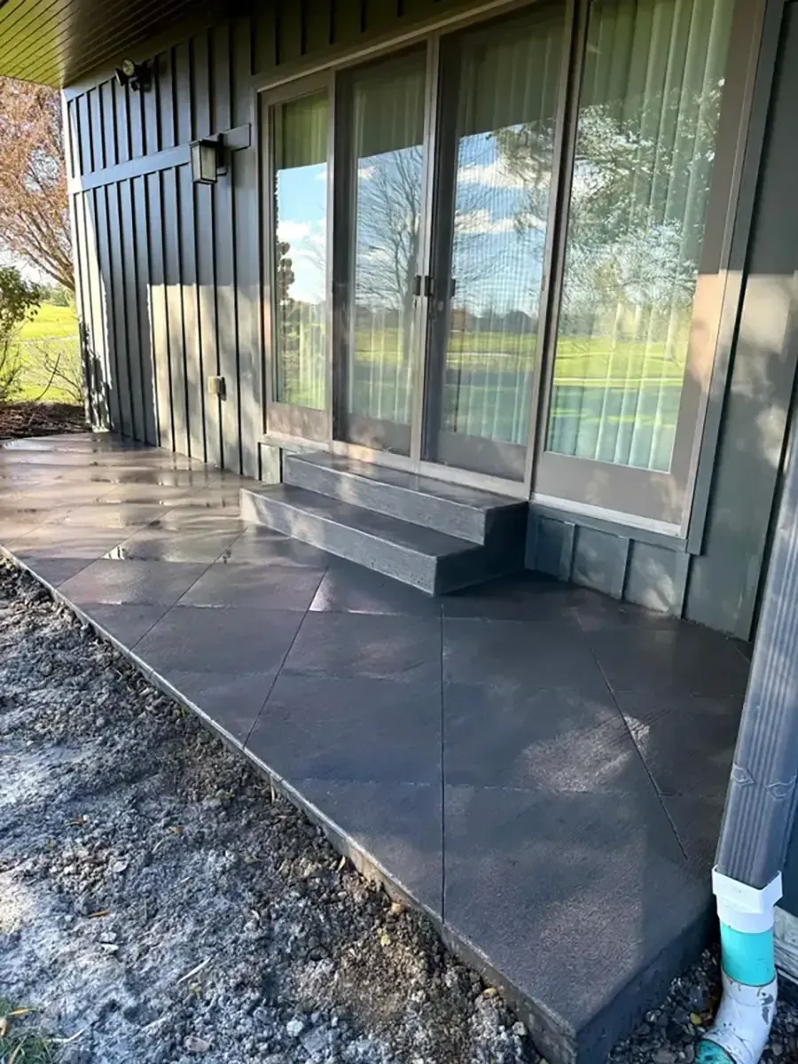Covered patio with dark tiled floor, sliding glass doors, and a gravel edge beside a house.