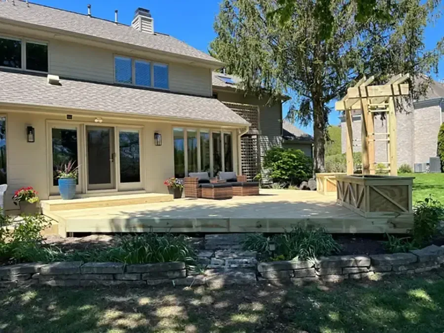 Backyard patio with sliding glass doors, potted plants, and a raised stone terrace under trees