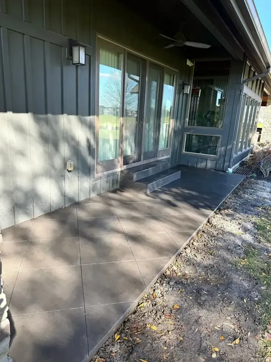 Concrete walkway beside a building with windows, casting tree shadows in sunlight