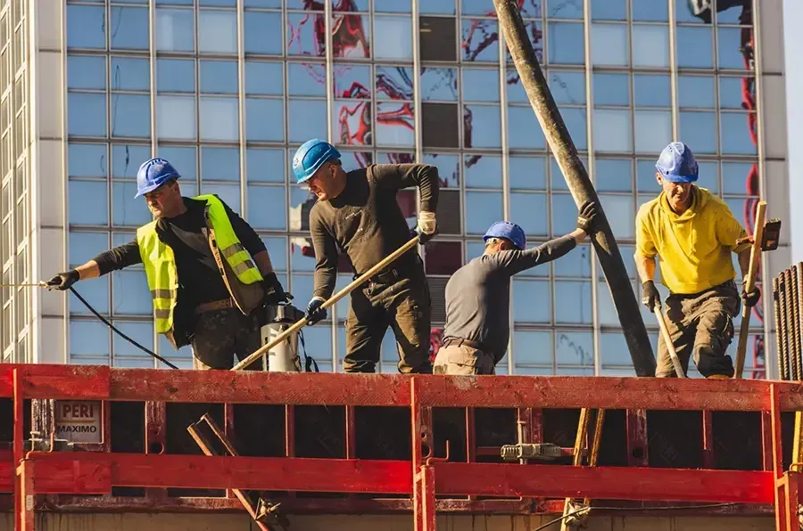 Construction workers on a red scaffold fixing steel rebar in front of a building facade