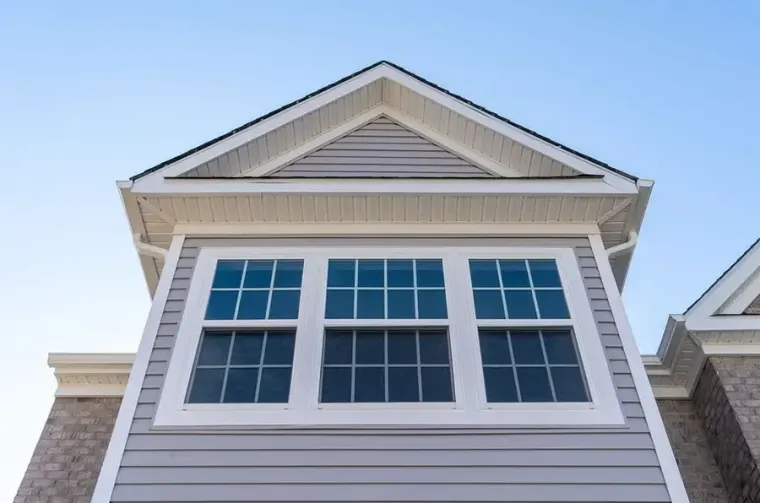 White house facade with three windows and a peaked roof against a blue sky