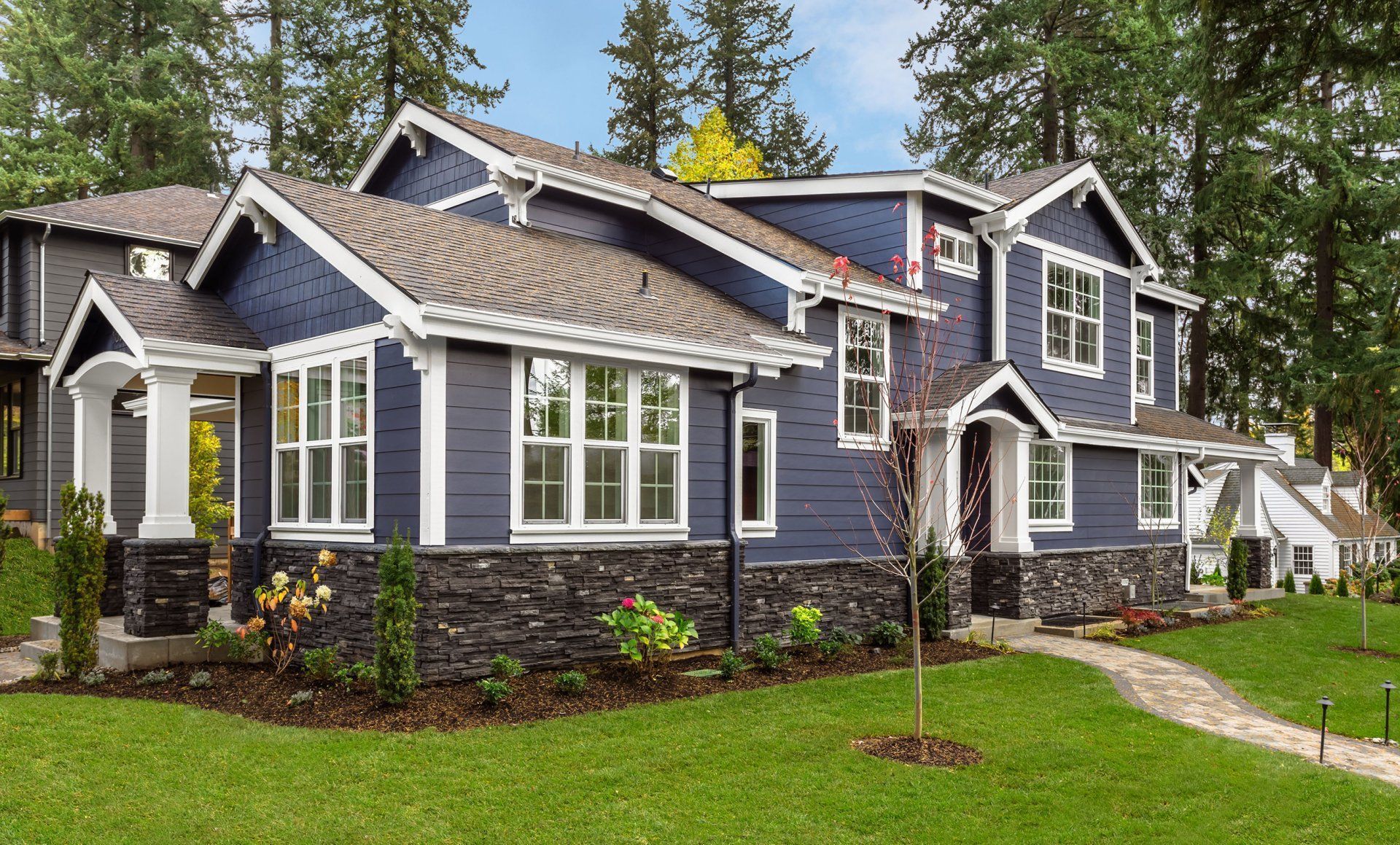 Gray two-story suburban house with stone accents, white trim, and a green lawn under tall trees