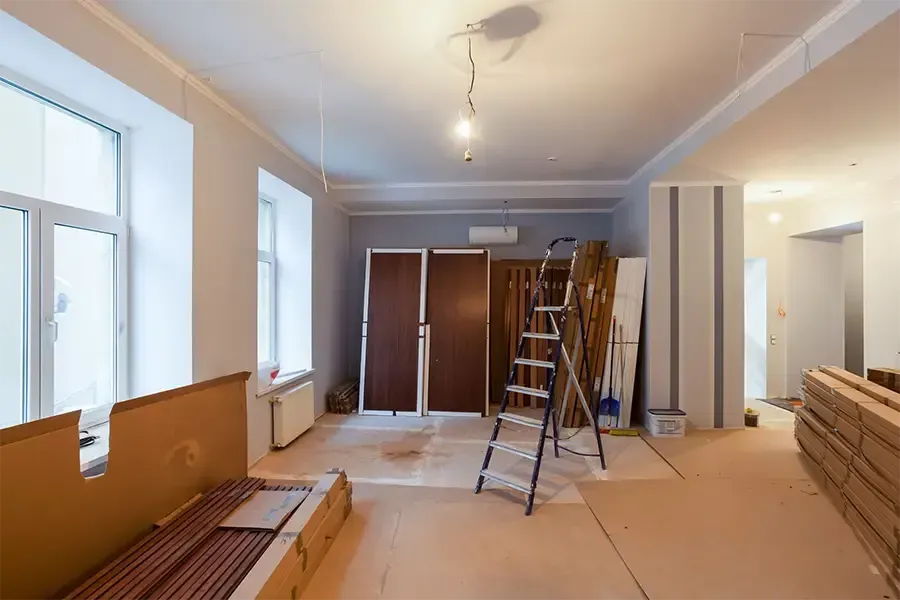 Partially renovated room with ladders, stacked wood, and tools under ceiling lights