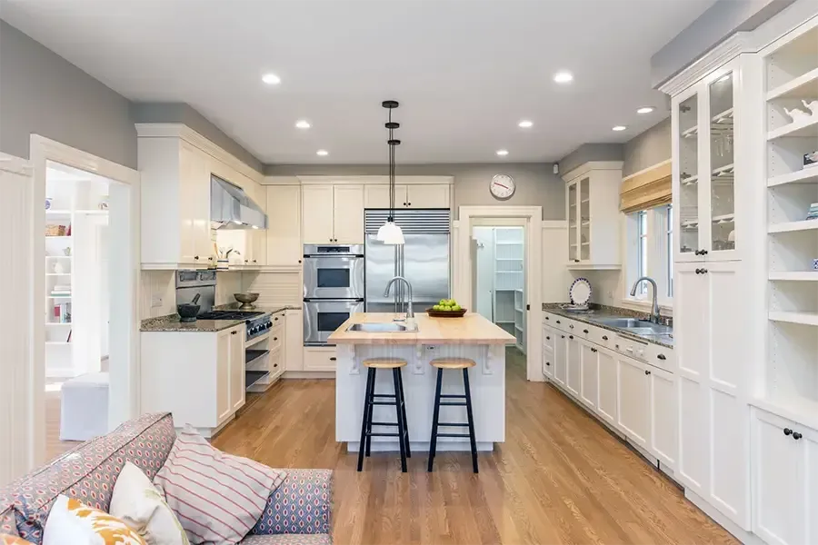 Bright modern white kitchen with island, bar stools, wood floors, and soft gray walls