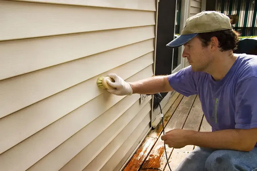 Person sanding beige siding on a house exterior with a hand sander