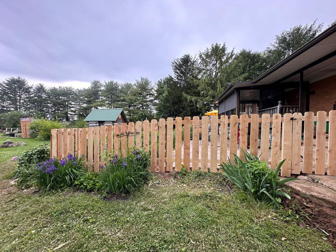 A wooden picket fence surrounds a garden in front of a house.