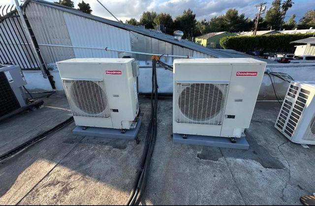 Two white outdoor HVAC units on a rooftop beside railings and a sloped walkway