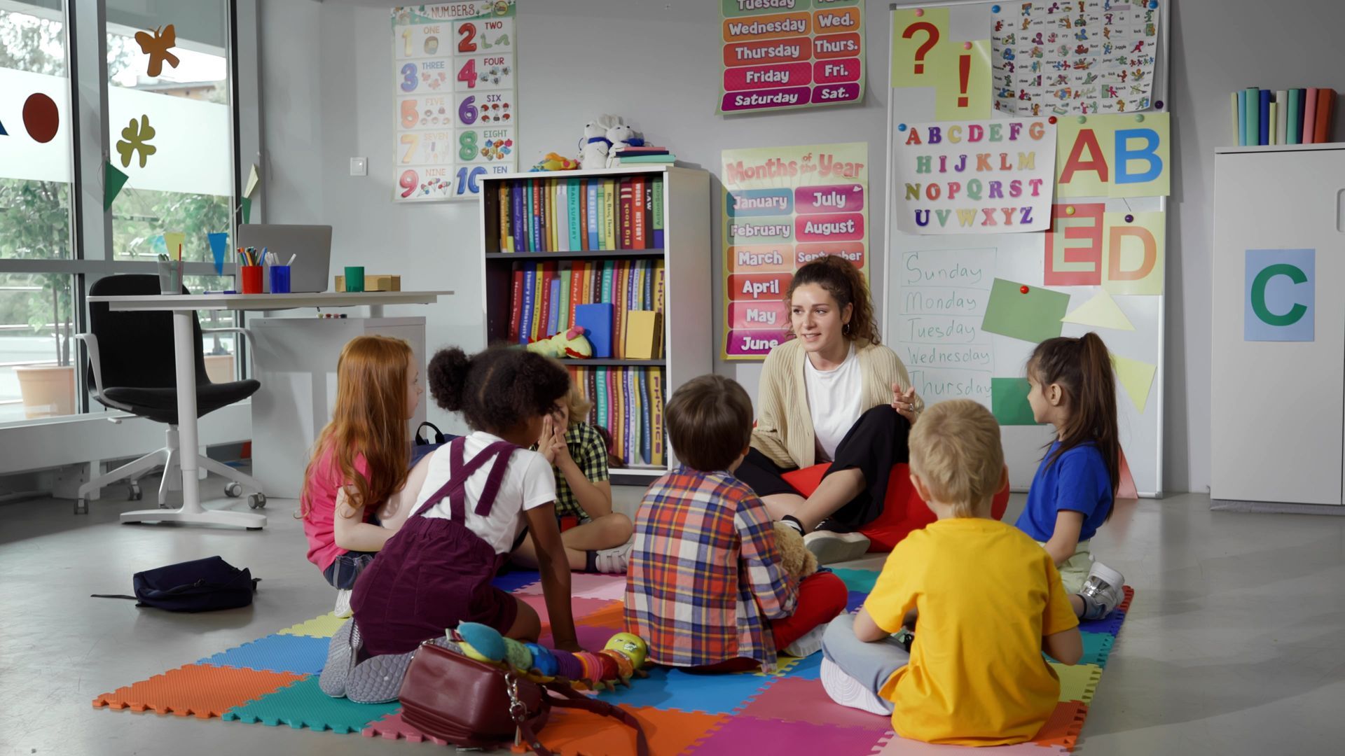 Children and a teacher are seated on the floor, having a lesson at a child care centre. Children and a teacher are seated on the floor, having a lesson at a child care centre.