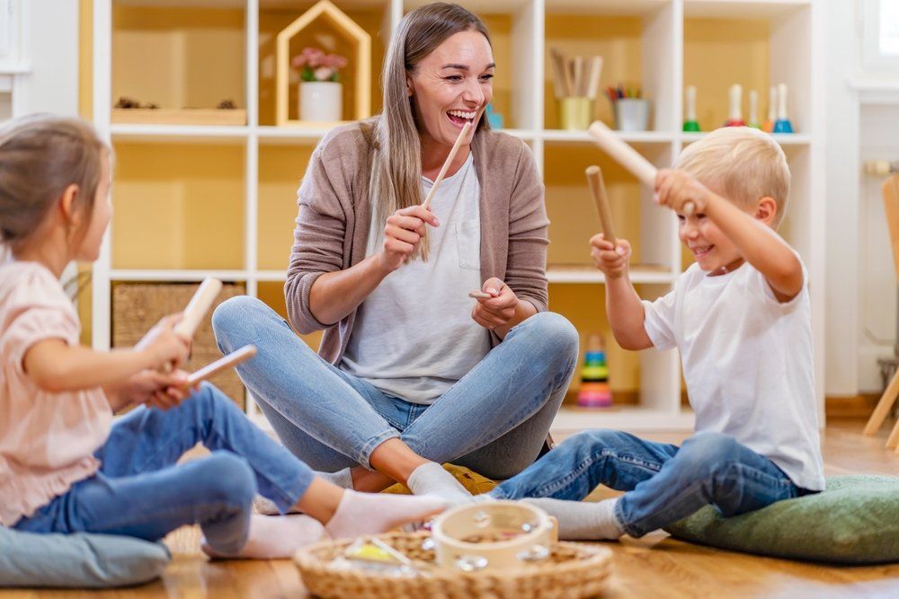 A woman and three children are sitting on the floor playing musical instruments. A woman and three children are sitting on the floor playing musical instruments.